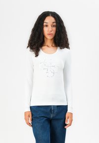 Weißes Langarm-T-Shirt mit einem kreisförmigen Design aus glitzernden Verzierungen auf der Vorderseite. Weiches, enganliegendes Material mit Rundhalsausschnitt.