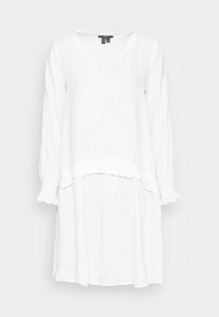 Vestido de lino blanco con escote en V y mangas largas. Presenta un dobladillo con volantes y puños elásticos. Textura suave y ligera.