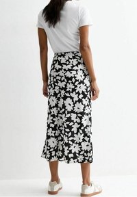 Gonna floreale in bianco e nero con un design fluido, caratterizzata da uno spacco sul retro. Abbinata con una t-shirt bianca e scarpe chiare.