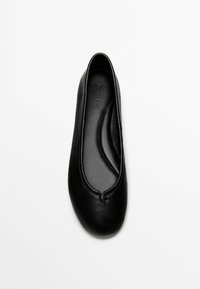 Zwarte lederen balletflat met afgeronde neus, kleine decoratieve knoop aan de voorkant en gevoerde binnenzool op een witte achtergrond.