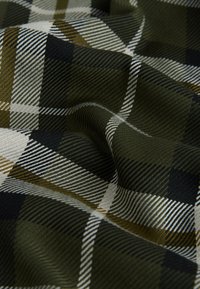 Tissu à carreaux vert foncé, noir, blanc et marron avec une texture tissée en diagonale et des plis doux.