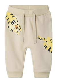 Beiga bomullsshorts med elastiskt midjeband, prydda med ett gult tigermönster på vänster ben och kontrasterande svarta ränder. Ribbad mudd.