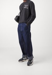 Černá mikina s bílým logem Adidas, doplněná volnými tmavě modrými džíny se bílým šitím. Černé tenisky s bílými akcenty.