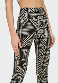Leggings de tiro alto fabricados con un tejido elástico que presentan un atrevido patrón geométrico en negro y beige con líneas y triángulos.