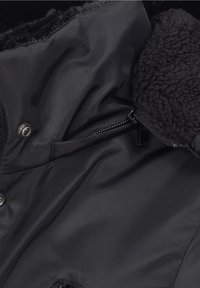 Czarna kurtka z pluszową, teksturowaną podszewką wewnętrzną, gładkim zewnętrznym materiałem, zamkiem błyskawicznym i ozdobnymi guzikami.