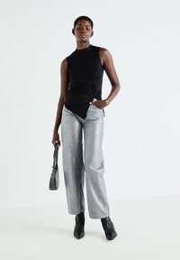 Top negru fără mâneci, cu detaliu legat, asortat cu blugi metalici argintii cu picioare largi. Modelul ține o geantă mică neagră și poartă botine negre cu vârful ascuțit.