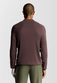 Maglione granata con texture a coste sulla parte superiore della schiena e delle spalle. Il design ha un taglio rilassato e un collo rotondo.