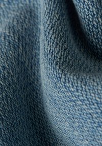 Světlá modrá džínovina s texturovaným povrchem, zobrazující tkané vzory a jemné odstínové variace. Měkký a mírně pomačkaný vzhled.