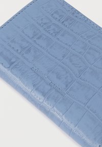 Hellblaues Portemonnaie mit glänzender Oberfläche und Krokodilhautstruktur. Das Design umfasst rechteckige Muster und dezente, eingeprägte Markenkennzeichen.