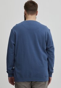 Sudadera azul con cuello redondo, mangas largas y una textura suave. Incluye detalles de costura sutiles en la parte posterior y puños de canalé.