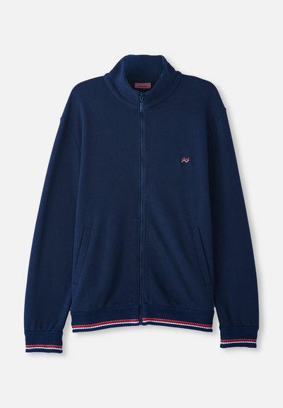 Temno modra jakna na zadrgo z visokim ovratnikom, rebrastimi manšetami in robom, ki vsebuje rdeče in bele črtne poudarke; narejena iz mehkega, teksturiranega materiala.