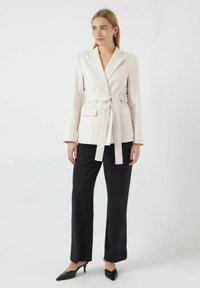 Lys pink skræddersyet blazer med bælte i taljen, to frontlommer og lange ærmer, parret med sorte brede bukser og hæle.