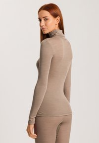Beige långärmad polotröja med en figurnära design och slät textur, visad på en modell i profil mot en ljus bakgrund.