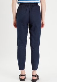Pantalon ajusté léger bleu marine avec une taille élastique, deux poches arrière et une texture lisse. Stylé avec un haut rayé.