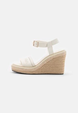 Hvid kile-sandal med vævet jutefod, ankelrem med spænde og åben tå med mærket stofrem over foden.