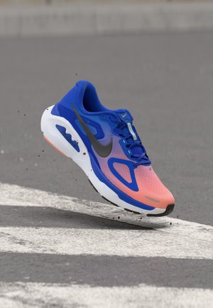 Μπλε και ροζ παπούτσι για τρέξιμο Nike στον αέρα πάνω από άσφαλτο με λευκές οδικές σημάνσεις, εμφανίζοντας λεπτομέρειες της σόλας και του λογότυπου στο πλάι.