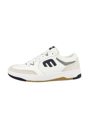 Baskets blanches avec des accents beiges et un logo noir. Présentent une texture perforée, des lacets plats et une semelle robuste avec un fond en caoutchouc naturel.