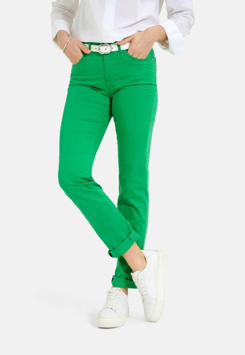 Pantalon en coton vert avec une coupe ajustée, revers retroussés et une ceinture blanche. Associé à des baskets blanches, la tenue comprend une chemise blanche rentrée.