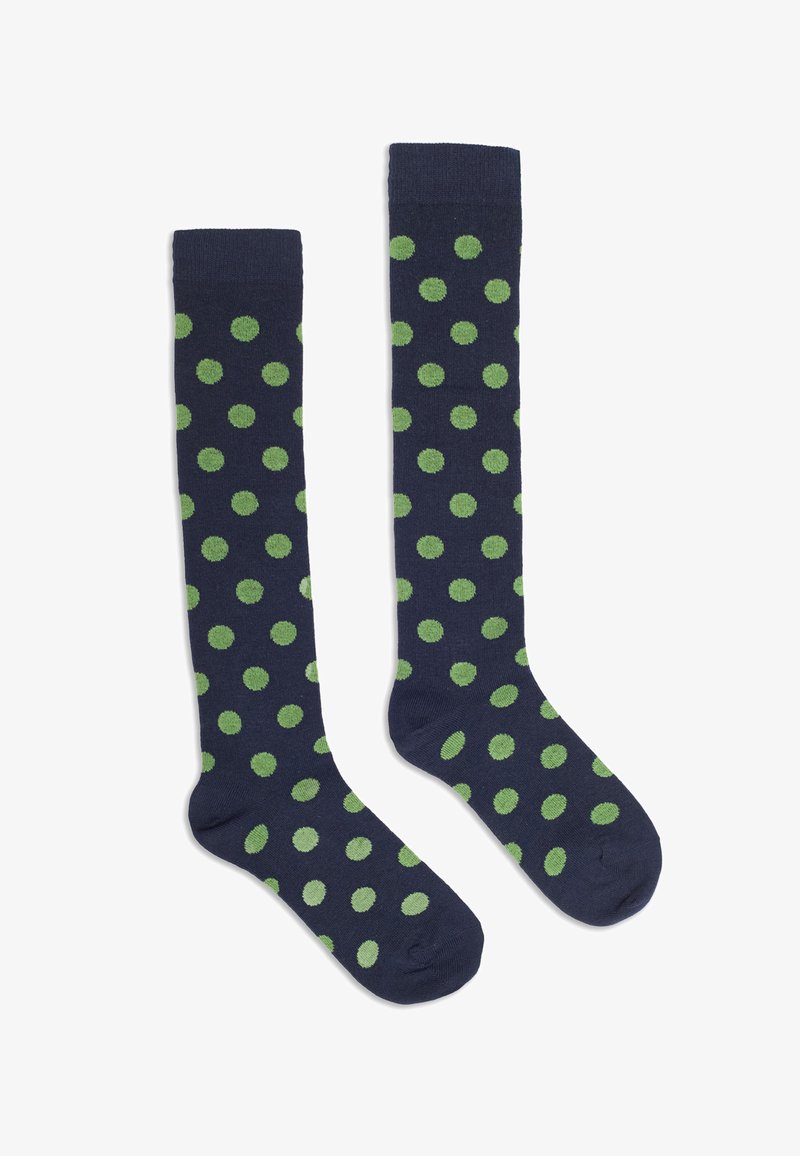Une paire de chaussettes bleu marine montantes avec des pois verts régulièrement espacés, posées à plat sur un fond blanc.