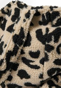 Fluffy bež tkanina s crnim uzorkom leoparda i mekanom teksturom. Dizajn uključuje nepravilne oblike i teksture.