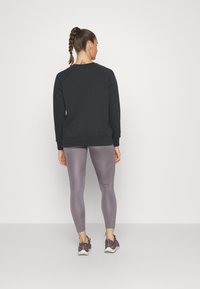 Sudadera negra y leggings gris claro, con una textura suave. Vista trasera que muestra una coleta trenzada y zapatillas deportivas.