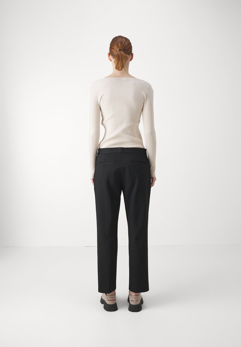 Kermainen ribbikuvioinen pitkähihainen paita ja mustat räätälöidyt housut. Paidassa on leveä pääntie; housuissa on slim fit -malli, jossa on takataskut. Mustat kengät.