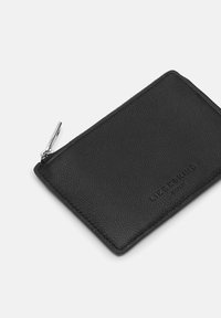 Czarny skórzany portfel na karty o fakturowanej powierzchni, z metalowym zamkiem błyskawicznym i wytłoczonym logo marki z jednej strony. Prostokątny kształt, smukły design.