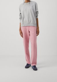 Sudadera gris con puños acanalados, combinada con unos vaqueros rectos de color rosa claro. El calzado consiste en zapatillas deportivas azul oscuro con acentos azules.