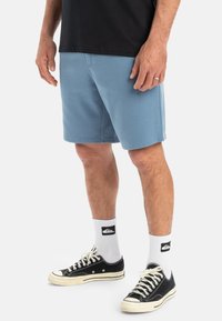 Lichtblauwe sportshorts met een gladde textuur, een elastische tailleband en zijzakken, gecombineerd met zwarte sneakers en witte sokken.