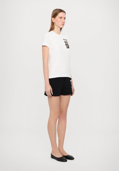 Camiseta blanca de manga corta con un gráfico de panda en el pecho, combinada con pantalones cortos negros y bailarinas negras. Diseño sencillo y casual con una paleta de colores básica.