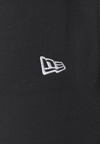 Melns audekla cepures modelis ar baltu izšūtu logotipu ar ģeometriskām dizaina detaļām, kas novietots priekšpusē. Mīksts materiāls, strukturēta forma.