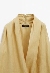 Leinen-Wickeloberteil in einem sanften Beigeton mit tiefem V-Ausschnitt und subtiler Textur. Verfügt über ein Etikett mit dem "Massimo Dutti"-Logo am Ausschnitt.