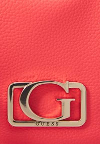 Borsa a mano in pelle corallo con un evidente logo "G" dorato, caratterizzato da una cornice rettangolare e una superficie testurizzata.