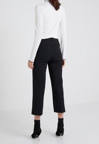 Pantalon noir sur mesure avec poches latérales, longueur raccourcie, texture lisse, associé à un haut blanc à manches longues côtelé et des bottines noires.