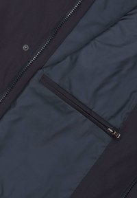 Wnętrze granatowej kurtki z gładkim materiałem, pełnowymiarowym zamkiem błyskawicznym i kieszenią na zamek. Teksturowana zewnętrzna warstwa dodaje kontrastu.