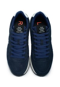 Sneakers in suede blu navy con tomaia testurizzata, lacci piatti, dettagli in bianco sulla suola e suola in gomma nera; presentano il testo "CORRI PIÙ VELOCE DI QUANTO PUOI" sulle sole interne.