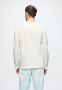 Camisa de manga larga color crema con cuello redondo, hecha de una tela suave. Estilo de corte relajado y combinada con pantalones de mezclilla en un tono azul claro.