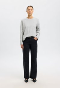 Grijs shirt met lange mouwen gecombineerd met zwarte wijde jeans met hoge taille. De outfit wordt aangevuld met zwarte ballerina's en een zwarte riem.