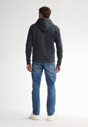 Felpa grigia scura con un grande logo sul retro, abbinata a jeans blu e sneakers bianche. Presenta un cappuccio con cordoncino e polsini a coste.