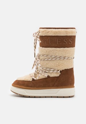 Rudos ir kreminės spalvos kailiniai auliniai batai su zomšos ir dirbtinio kailio apdaila. Ypatybės: tekstūruotas paviršius, prekės ženklą atitinkantis akcentas ir masyvus baltas padas.