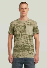 Groen camouflagepatroon T-shirt met een ronde hals en korte mouwen; heeft een effen groene zak op de linkerkant van de borst.