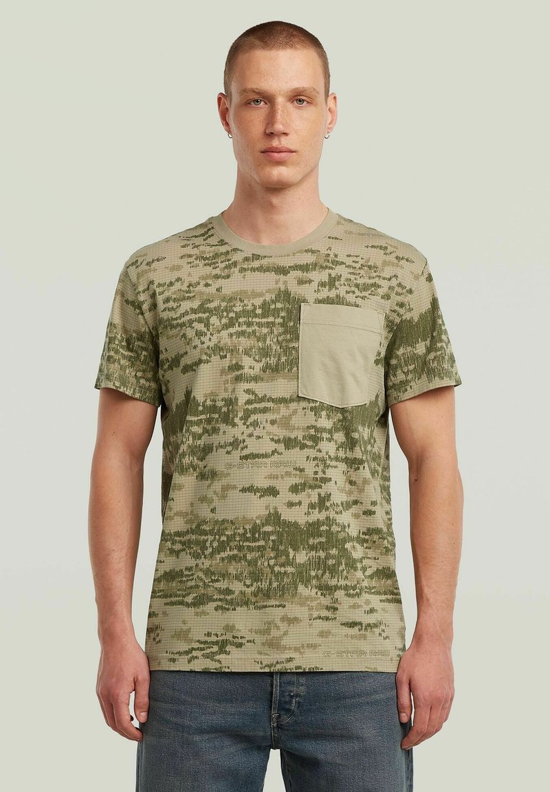 Groen camouflagepatroon T-shirt met een ronde hals en korte mouwen; heeft een effen groene zak op de linkerkant van de borst.