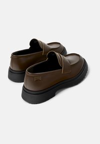 Mocasines de cuero marrón con puntera redondeada, una tira cosida en la parte delantera y una suela gruesa de goma negra. Presentan un detalle de logo en el lateral.