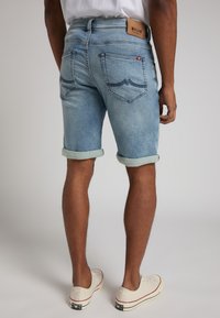Shorts en denim bleu clair, avec des ourlets roulés, des poches arrière avec des détails de couture et une étiquette en cuir marron portant l'inscription "MISTING".