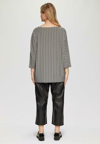 Zwart-wit gestreepte top met een brede halslijn en driekwart mouwen, gecombineerd met zwarte leren cropped broek en zwarte schoenen.