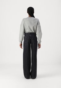 Grå sweatshirt med sänkta axlar, ihop med svarta vida jeans med bakfickor och hög midja. Enkelt design, avslappnad look.