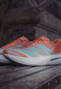 Koralowe i niebieskie buty do biegania z białymi podeszwami i logo "Lightstrike Pro" umieszczone na teksturowanej, drewnianej powierzchni na zewnątrz.