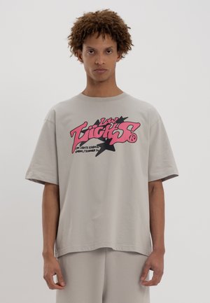 Un tricou oversized de culoare gri deschis, cu un logo grafic îndrăzneț în nuanțe de roz și negru pe partea din față. Fabric din bumbac moale, decolteu rotund, croială lejeră.