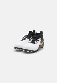 A Nike focicipők túlnyomórészt fehér felsőrésszel rendelkeznek, fekete részletekkel és arany színű Swoosh logóval. A dizájn texturált mintákat és fekete fűzőket tartalmaz.