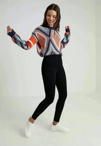 Jersey de colores multicolores con diseños geométricos, combinado con jeans skinny negros de cintura alta y zapatillas blancas.